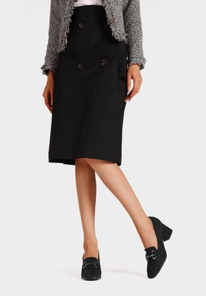 Gonna a matita nera con dettagli di bottoni doppi, realizzata in tessuto testurizzato, abbinata a scarpe nera con tacco a blocco e hardware decorativo.