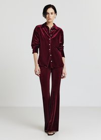 Set di camicia e pantaloni in velluto bordeaux. La camicia presenta un colletto e bottoni frontali; i pantaloni sono aderenti e svasati sul fondo.