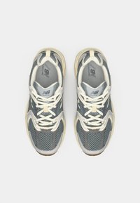 Gray athletic sneakers with a mesh upper, cream laces, and rubber soles. Notable details include layered design and logo on the tongue.