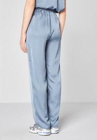 Světle modré saténové kalhoty s elastickým pasem, volného střihu a rovnými nohavicemi, doplněné šedými sportovními botami.