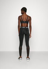 Black athletic outfit featuring a bralette with a Nike logo and black leggings with mesh accents, showcasing a fitted design and stretch material.