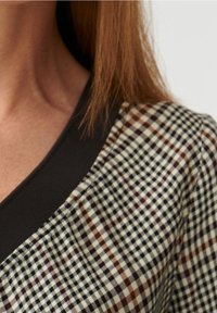 Camicia button-up con un motivo a quadri in crema, bordeaux e blu navy. Collo a costine marrone scuro aggiunge texture e contrasto.