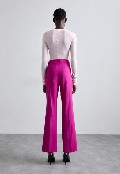 Vaaleanpunainen pitkähihaisten paito, jossa on takasauman yksityiskohta, yhdistettynä korkeavyötäröisiin, avara-jalkoisiin kirkkaanpunaisiin housuihin ja mustiin korkokenkiin.