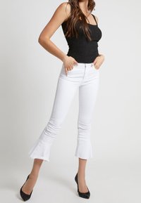 Top in cotone nero a costine, jeans bianchi a campana con orli grezzi e tacchi a punta neri. Design aderente, texture liscia.