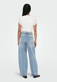 Top bianco a coste con maniche a volant in pizzo abbinato a jeans azzurri chiari, a gamba larga e sbiaditi. Colore solido con dettagli di design minimalisti.