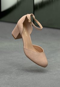 Bezsűrű velúr magassarkú cipő lekerekített orral, boka pánttal és vastag sarokkal, sima textúrával és minimalista dizájnnal.