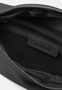 Borsa in pelle nera con chiusura a zip, con un interno liscio e una piccola etichetta di tessuto con la scritta "FREDsBRUDER". Dettaglio esterno con texture.