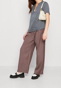 Top blu navy con motivo a rombi bianchi, maniche corte; pantaloni larghi marroni a vita alta; scarpe con platform bianche e nere; piccola borsa crema.