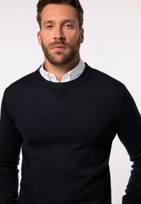 Marineblauer Rundhals-Pullover aus feinem Strickmaterial, mit strukturiertem Stitch-Detail an der Schulter und einer figurschmeichelnden Silhouette.