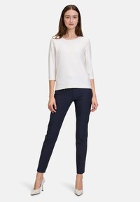 Vit texturerad topp med trekvartslånga ärmar, kombinerad med figurnära marinblå byxor och beige höga klackar. Enkel, modern design med neutrala färger.