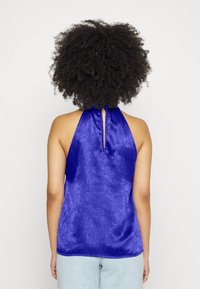 Top halter em cetim de um vibrante azul royal com um detalhe em fenda nas costas. Textura suave e um corte ligeiramente solto.