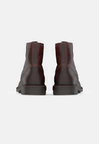 Botas de tobillo de cuero marrón con una textura suave, punta redondeada y costuras en contraste. Suela de goma duradera con detalles de dibujo.