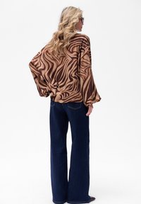 Bruine en tan lange mouwen blouse met een spiraalpatroon, gecombineerd met donkerblauwe wijde jeans, die een ontspannen silhouet toont.
