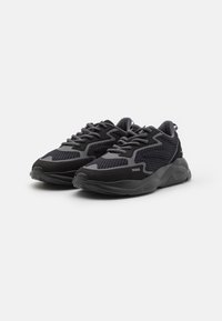 Scarpe da ginnastica nere realizzate in materiali mesh e suede, con suola spessa, dettagli grigi e tomaia testurizzata con lacci.