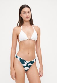Witte driehoekige bikini-top met dunne bandjes, gecombineerd met hoge bikini-bottoms met een groen-wit abstract patroon.