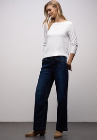 Hvid langærmet top kombineret med mørkeblå jeans med vide ben og beige ankelstøvler, med en glat tekstur og minimalistisk design.