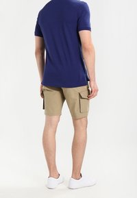 Camicetta a maniche corte navy, pantaloni cargo color khaki con tasche laterali e sneakers bianche. Vestibilità casual e comoda. Tessuto liscio.