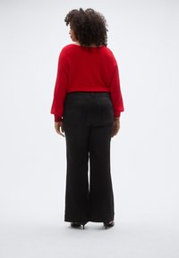 Pulover roșu cu dungi, cu mâneci largi, asortat cu pantaloni evazați negri cu talie înaltă. Textură netedă, croială casual, fără accente notabile.