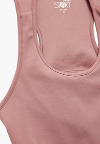 Top de deporte rosa claro hecho de una tela suave; presenta un cuello redondo, grandes sisas y detalles de costura mínimos. Tamaño pequeño.