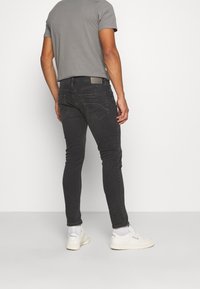 Vaqueros pitillo negros con un lavado desgastado, cinco bolsillos y costuras visibles. Combinados con una camiseta gris y zapatillas blancas.