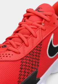 Rød atletiksko lavet af mesh og syntetiske materialer, med et sort Nike-swoosh, zigzag-mønster og flade snørebånd. Hvid sål.