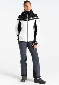 Winterjacke in Weiß und Schwarz mit Reißverschluss vorne, tailliertem Design und Kapuze. Kombiniert mit dunkelgrauen Hosen und robusten schwarzen Stiefeln.