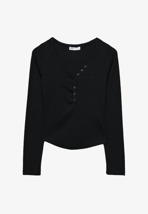 Haut noir à manches longues en tissu côtelé. Présente un décolleté en V et sept boutons noirs le long de l'avant, avec un ourlet arrondi.