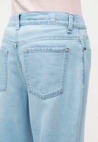 Ανοιχτό μπλε τζιν παντελόνι που φοριέται από ένα άτομο, εμφανίζοντας τις πίσω τσέπες, τις θηλιές της ζώνης, και μια μικρή ετικέτα μάρκας κοντά στη μέση.