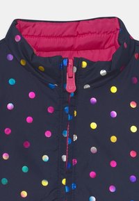 Navy jacket with multicolored metallic polka dots, a pink quilted collar, and a pink zipper. Smooth fabric with a shiny finish.