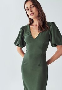 Grünes, enganliegendes Kleid mit tiefem V-Ausschnitt und Puffärmeln. Glattes Stoffmaterial mit subtiler Textur, enthält Seitennaht für eine formende Silhouette.