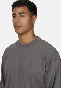 Szary długi rękaw sweatshirt z okrągłym dekoltem i delikatnym teksturowanym wykończeniem. Posiada małe, haftowane logo na piersi.