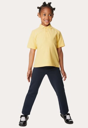 Gele korte mouwen polo, navybroek en zwarte schoenen. Het shirt heeft een kraag met drie knopen; de broek is tapered en heeft een gladde textuur.