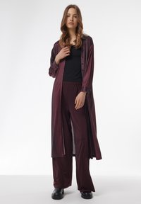 Camisa larga color burdeos con patrón de cuadros, combinada con pantalones holgados a juego, que cuentan con un corte relajado y una parte superior negra lisa debajo.