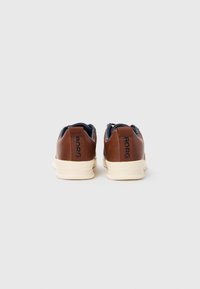 Baskets en cuir marron avec une semelle crème, présentant un intérieur marine et une marque "BORG" sur le talon. Texture lisse et design minimaliste.