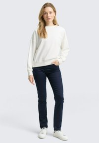 Weißer Pullover mit strukturiertem Rippdesign, lockerer Passform und Rundhalsausschnitt, kombiniert mit marineblauen geraden Hosen und weißen Sneakers.