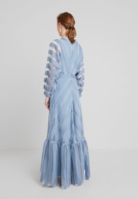 Ljusblå långärmad klänning med genomskinlig randig design, nyckelhål i ryggen, figurnära midja och volangkant. Maxilängd, flödande struktur.