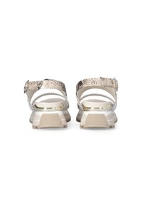 Des sandales beiges présentent une sangle texturée et à motifs avec une boucle métallique, une semelle rembourrée et un talon légèrement surélevé pour un meilleur soutien.
