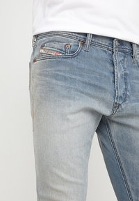 Jeans de mezclilla azul claro con diseño en degradado, cinco bolsillos y remaches de metal. Textura ligeramente desgastada en los paneles frontales.