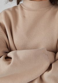 Beige polotröja i mjukt tyg med ribbad hals och vida, något överdimensionerade ärmar för en avslappnad passform.