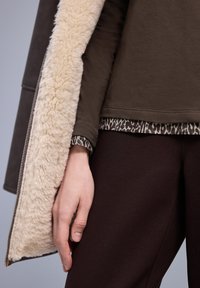 Bruine jas met beige namaakbontvoering, gecombineerd met een shirt met een donker luipaardpatroon en donkerbruine taps toelopende broek.