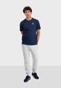Navy blue t-shirt with short sleeves, paired with light gray sweatpants. Black athletic shoes with red and white accents. Casual fit.