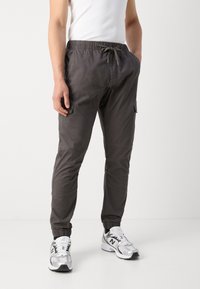 Pantalon cargo gris foncé en tissu léger, avec une taille élastique à cordon de serrage, une poche latérale et des revers effilés.