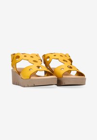 Sandalias de cuña de cuero amarillo con diseño recortado, suela de plataforma beige y fondo texturizado. Diseño de punta abierta, estilo con tiras y acabado suave.