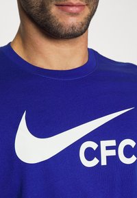 Niebieska bawełniana koszulka z dużym białym logo Nike i napisem "CFC" w pogrubionym stylu. Krój z okrągłym dekoltem o gładkiej fakturze.