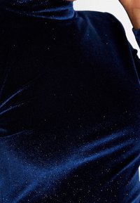 Haut col roulé en velours bleu marine avec une texture douce, orné d'accents de paillettes subtiles créant un effet scintillant.