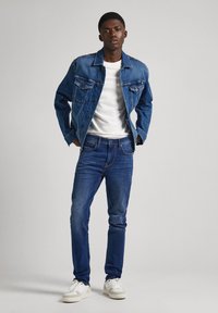 Keskmise pesu denim-jakk rinnataskutega, kombineeritud valge T-särgi ja tumedate siniste teksadega. Jalatsiteks sobivad spordijalatsid.
