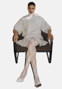 Grijze oversized sweatshirt met een hoge kraag, gelaagde roezelrok, kantkousen en witte hakken. Model zittend in een stoel.