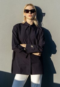 Navy long-sleeve shirt featuring a classic collar and star-shaped silver hardware on the cuffs, paired with white trousers.