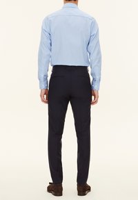 Hellblaues Hemd mit langen Ärmeln, kombiniert mit dunkelblauen Hosen. Glattes Material, taillierte Passform und dezente Stickdetails.