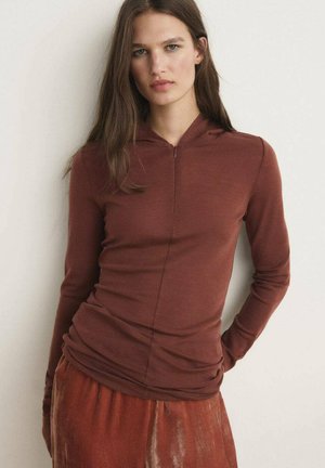 Dlhý rukáv, rustovo sfarbený top so zipsom na krku. Tkanina je hladká a priliehavá, skombinovaná s drapovanou, doplnkovou sukňou.
